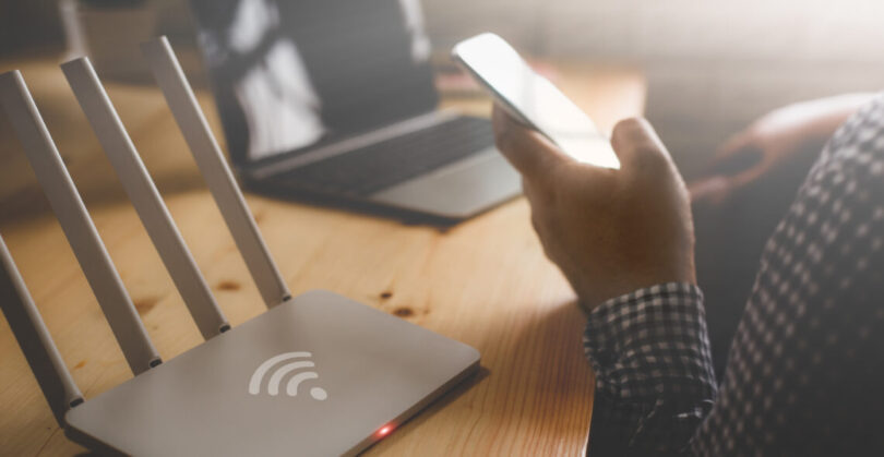 Closeup Of A Wireless Router And A Man Using Smartphone On Livin
