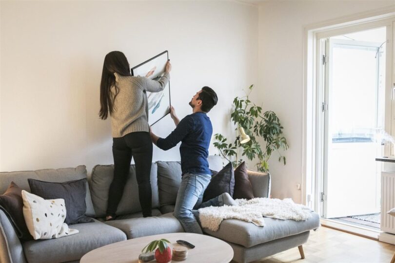 Couple adjusting painting on wall while leaning on royalty free image 953941956