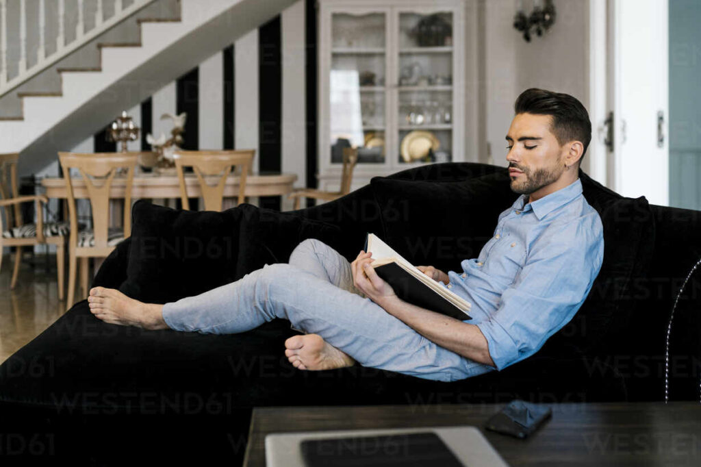 Valencia, Spain. Man Lying On The Sofa At Home Reading A Book.